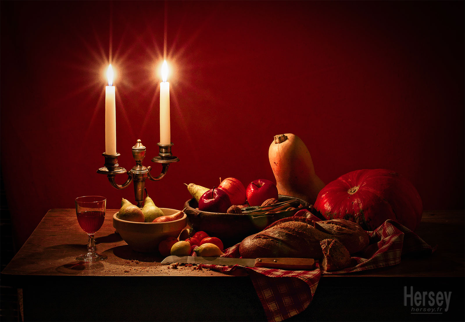 Nature morte d'hiver fruits de saison bougies pain citrouille pommes poires citrons mandarines verre de vin sur une table de cuisine © Hersey Photographe